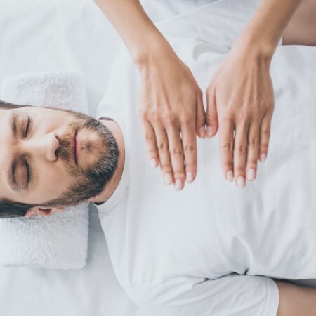 top view of bearded man with closed eyes receiving reiki treatment